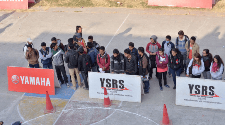 A group of people gathered around a motorcycle safety training area with cones and signs for yamaha and ysrs (yamaha safety riding science) in nepal.