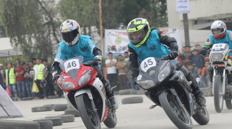 Two motorcycle racers, numbered 46 and 45, intensely compete in a motorbike race as they take a sharp turn, leaning deeply into the corner with a crowd and other competitors in the background.